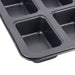 A close-up of a dark gray non-stick 6-compartment muffin or cupcake pan, showing the textured interior of the compartments and the raised rim, set against a plain white background.