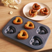 De Buyer six-cup non-stick heart-shaped cake tray with three baked heart-shaped cakes cooked in the tray, alongside a plate with three decorated cakes with clear and red drizzle glaze on a white plate.